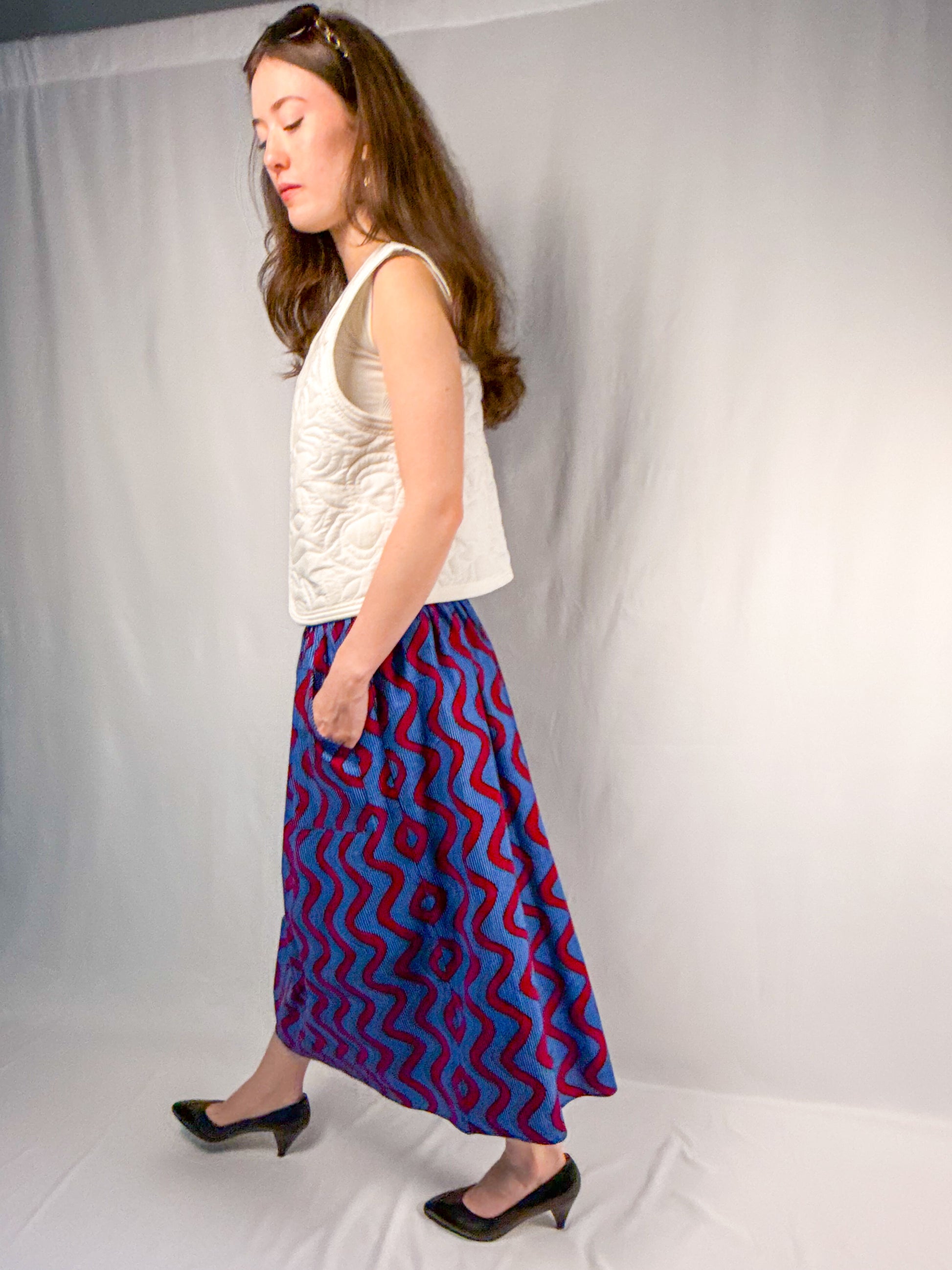 Woman wearing a white top and blue and red patterned skirt against a plain background