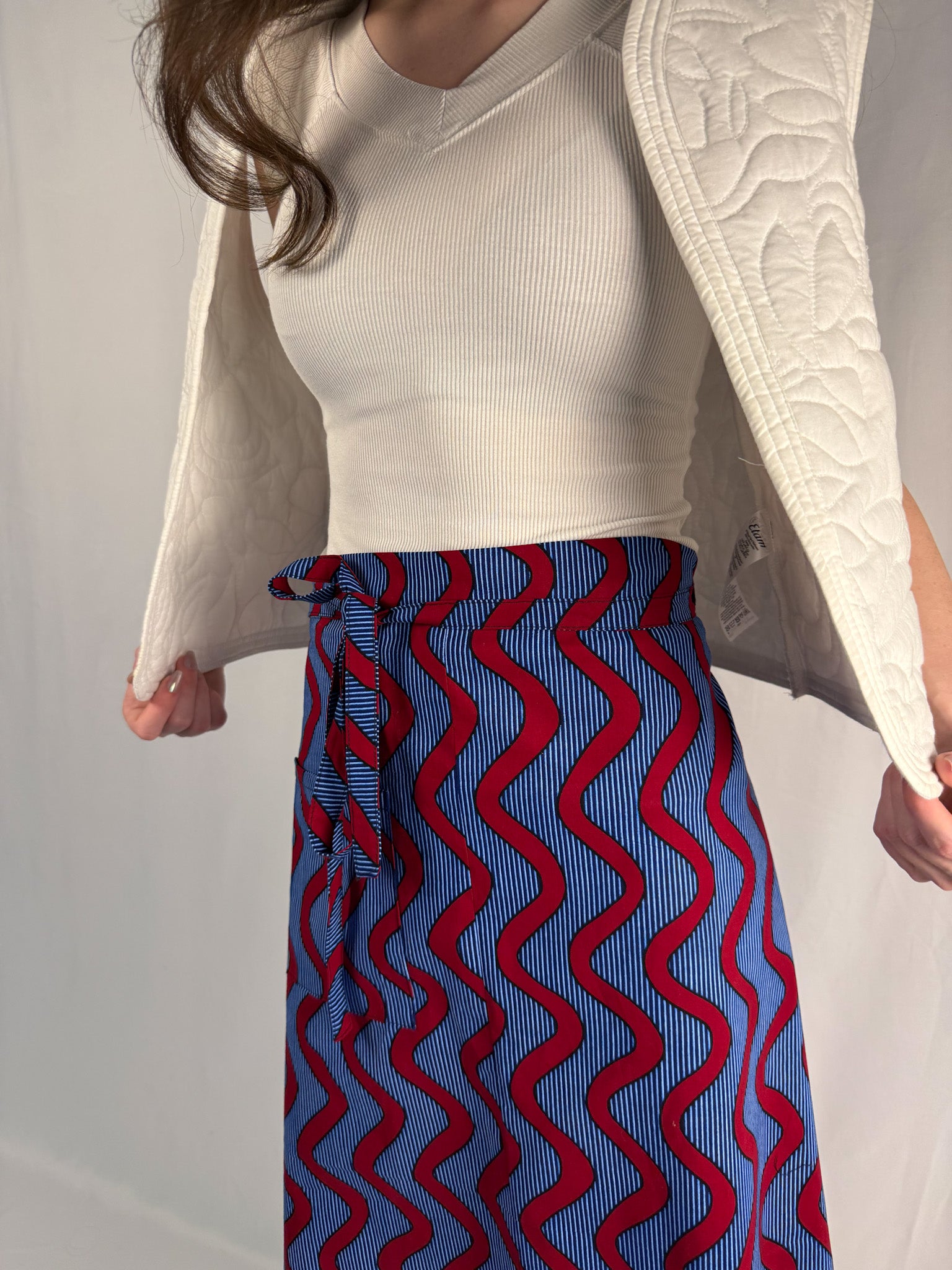 Person wearing a white top and blue and red patterned skirt against a plain background