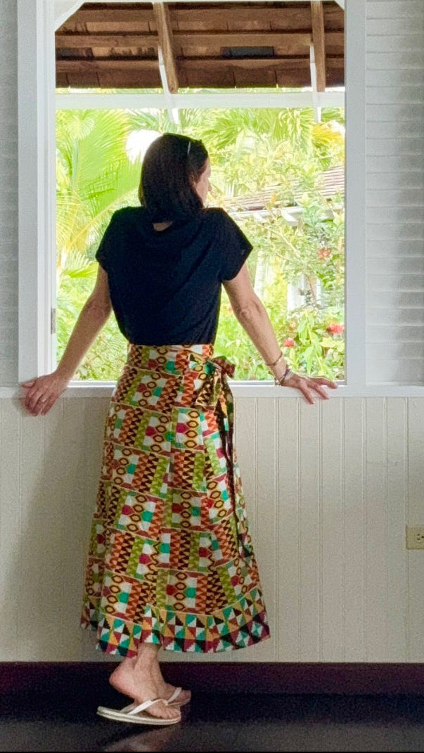 Woman in a colorful skirt standing by a window with a view of greenery.