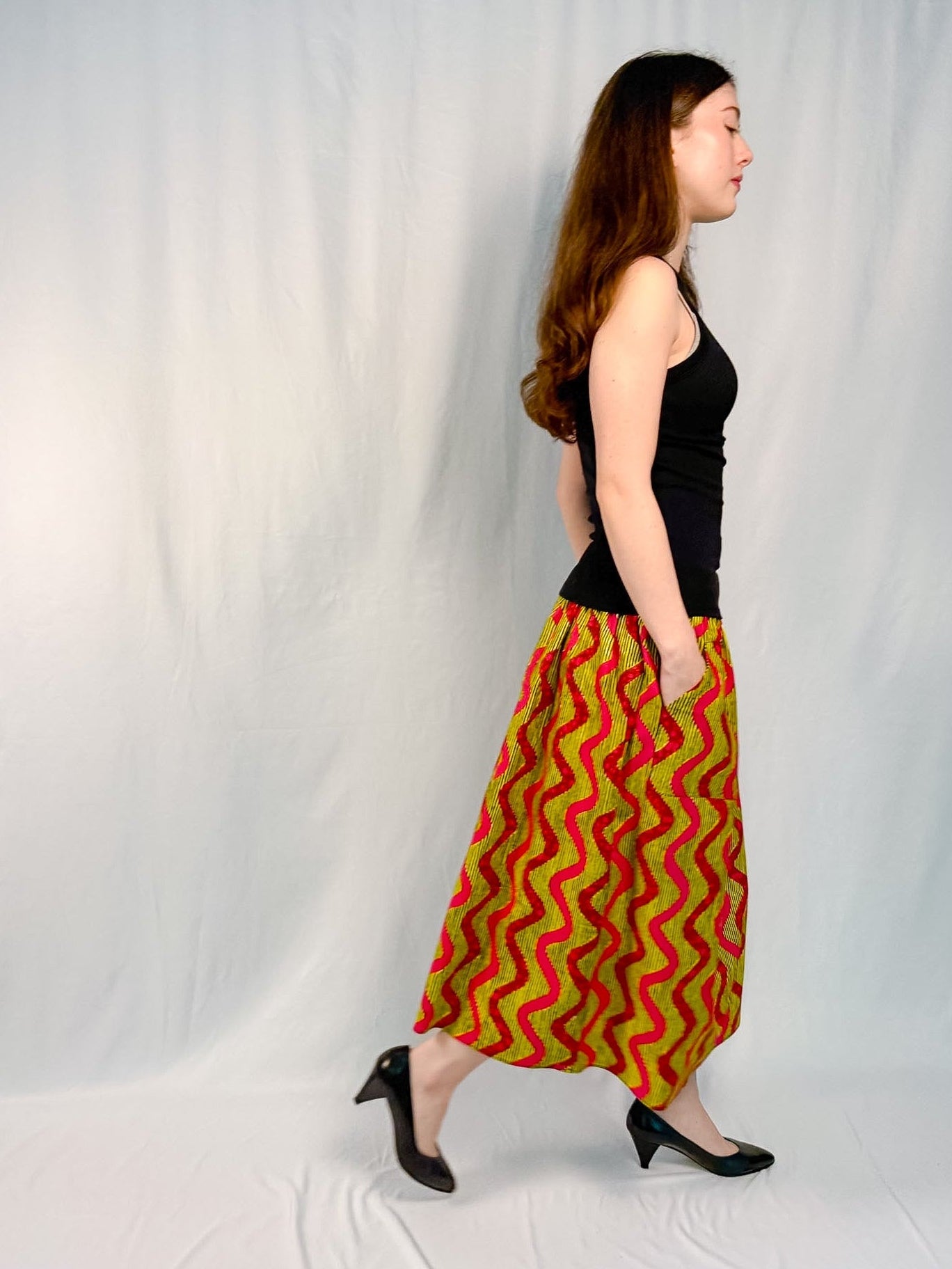 Woman wearing a black top and red and green patterned skirt on a white background