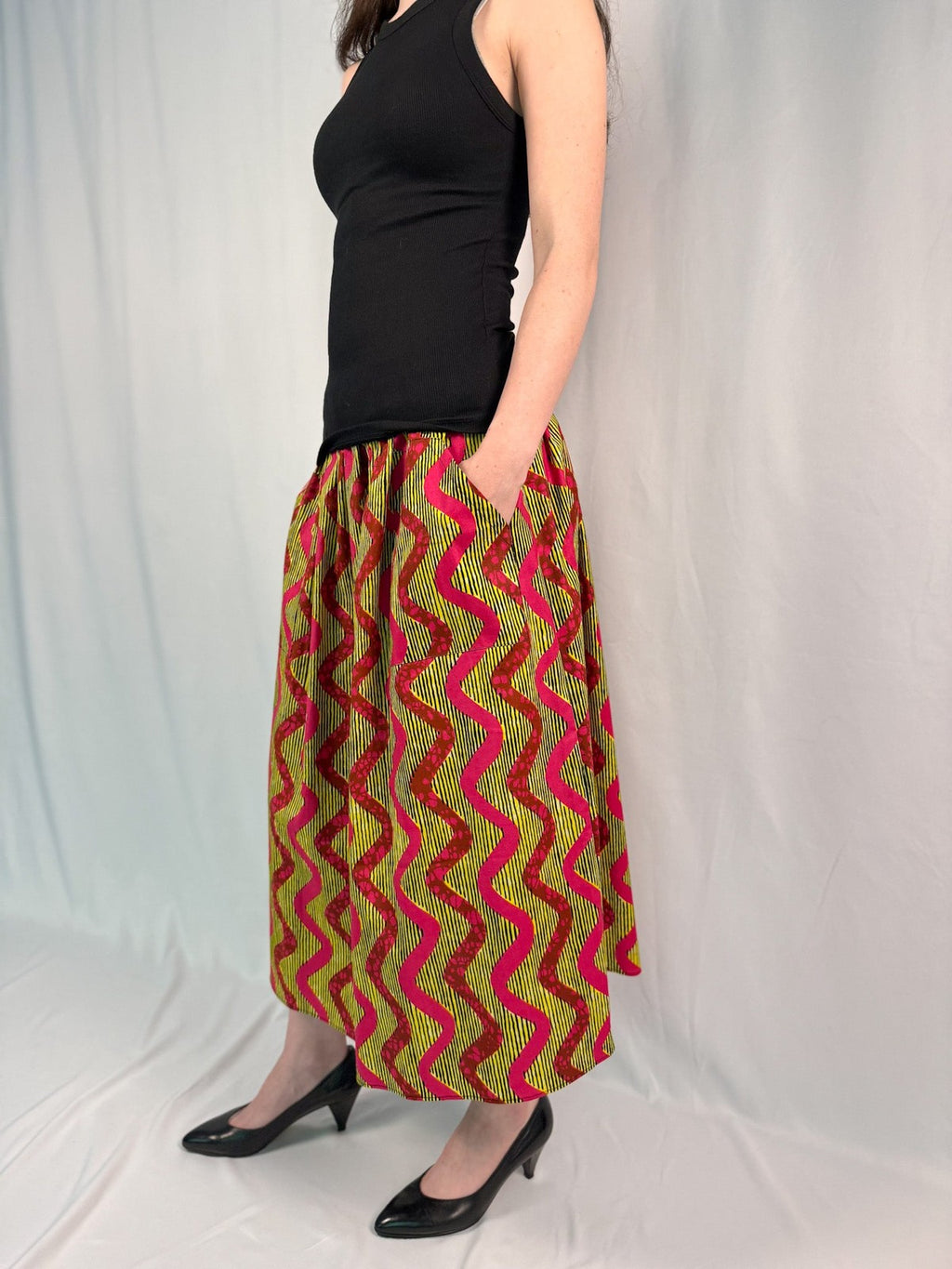 Person wearing a black top and colorful zigzag patterned skirt on a white background onsem