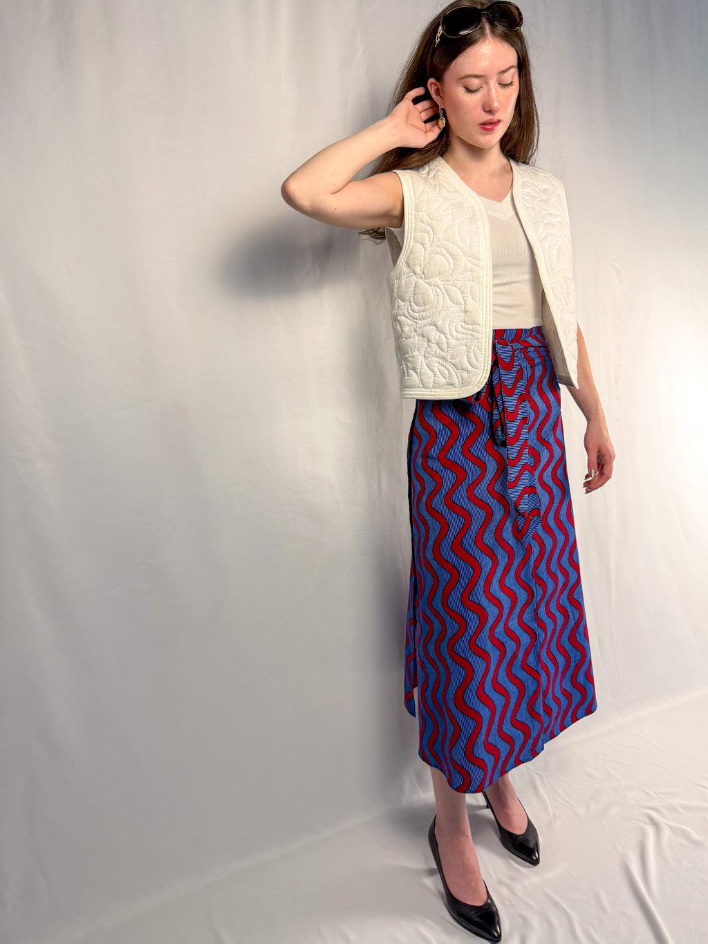 Woman wearing a white vest and blue patterned skirt against a plain background