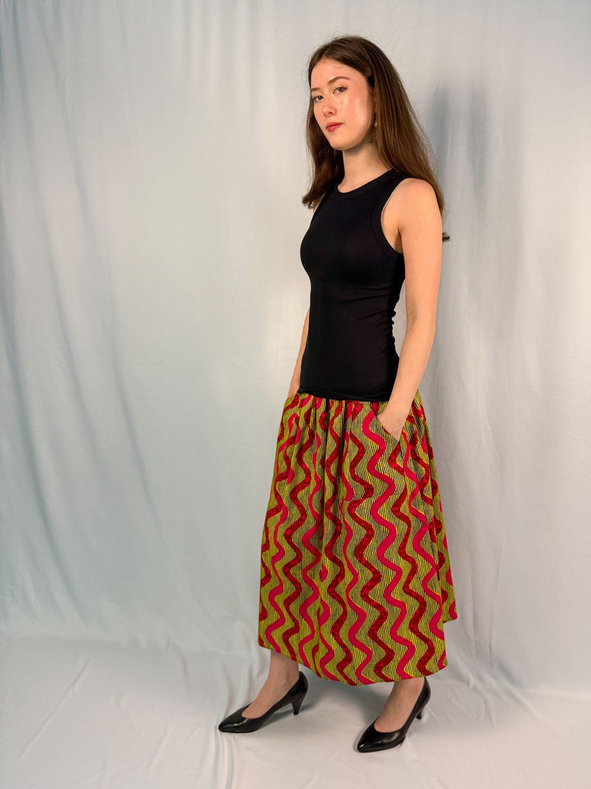 Woman wearing a black top and patterned skirt against a plain background onsem