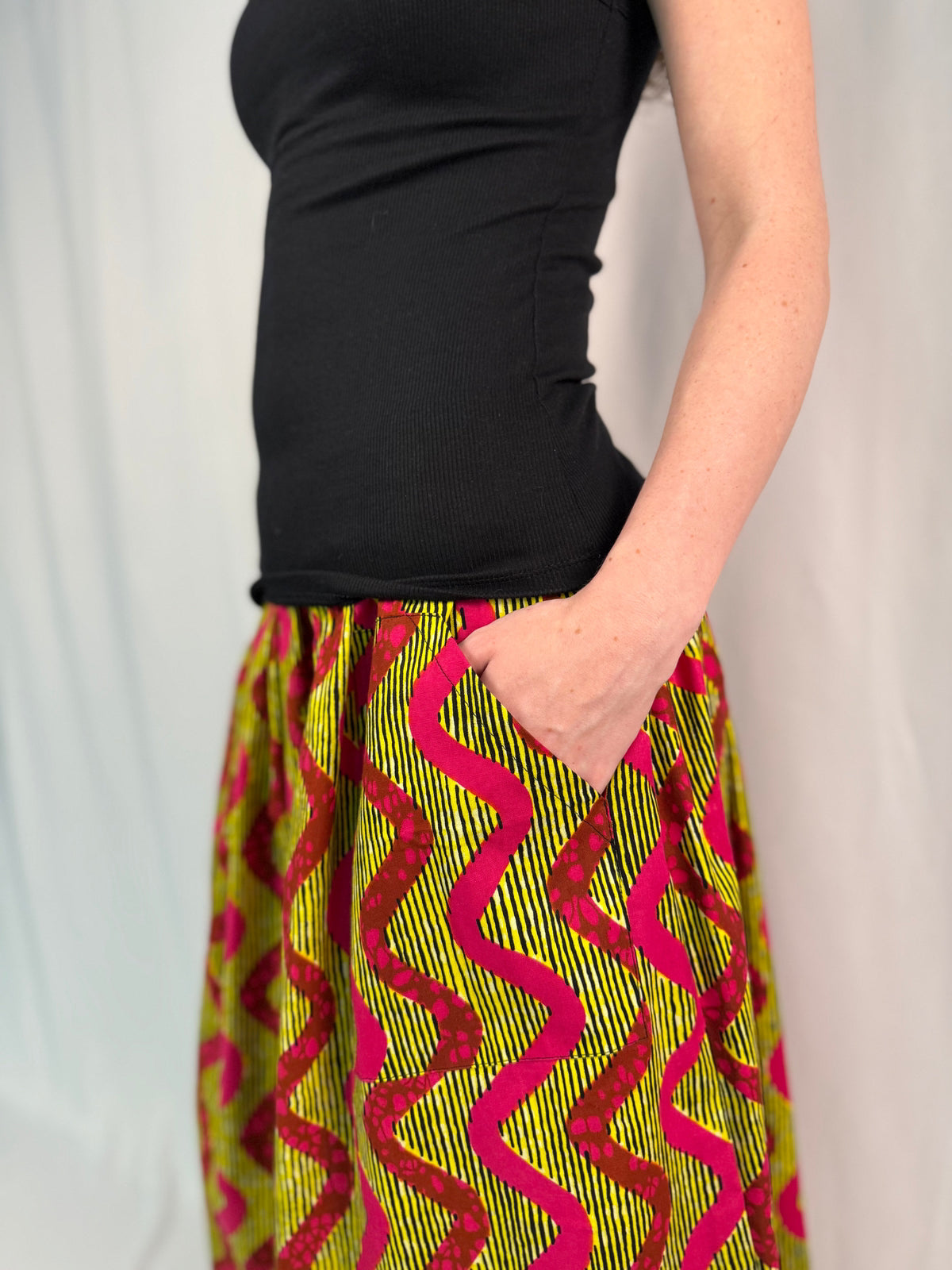 Person wearing a black top and colorful pin and yellow patterned skirt 