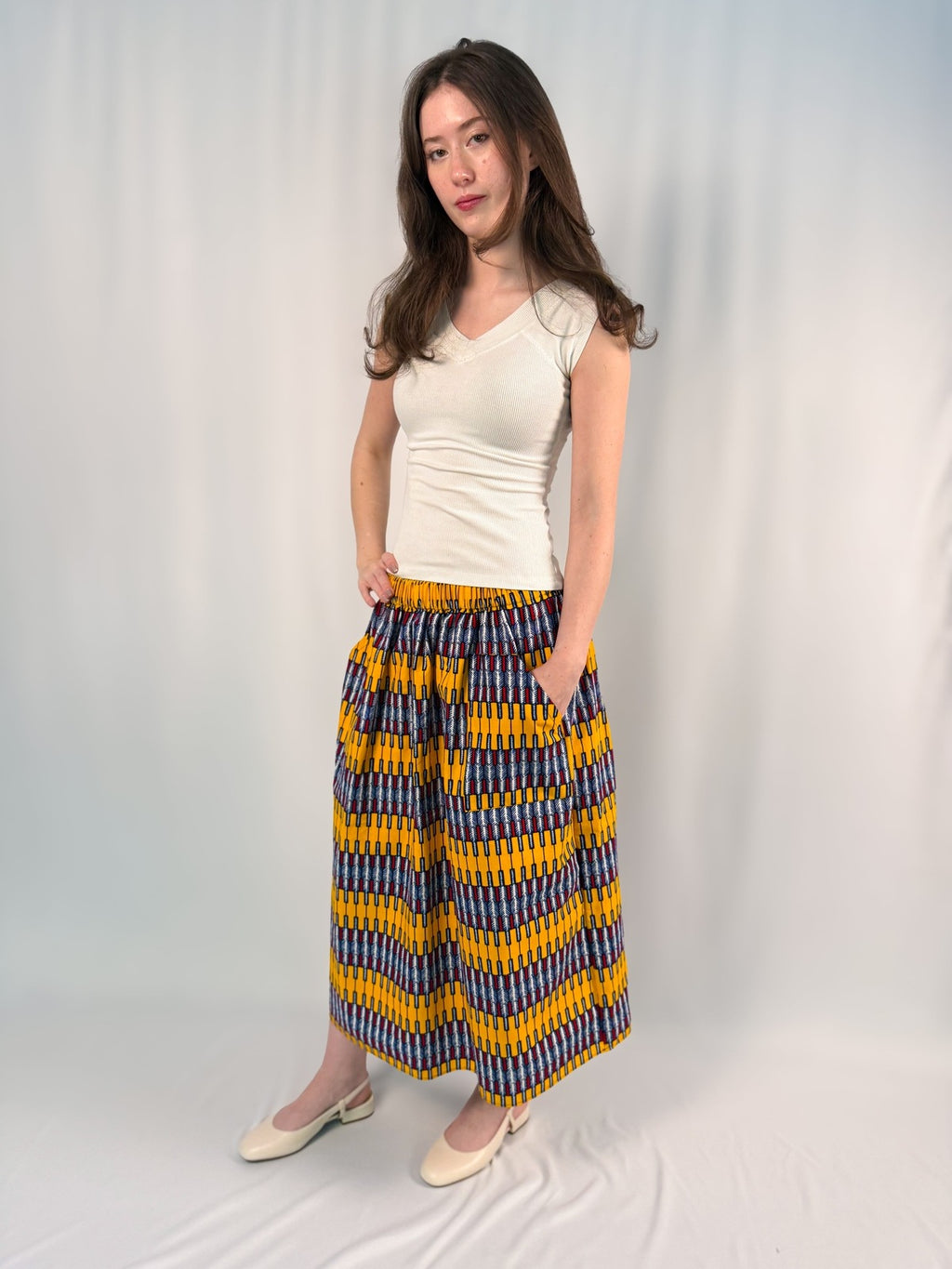 Woman wearing a white top and colorful patterned pants on a plain background - onsem