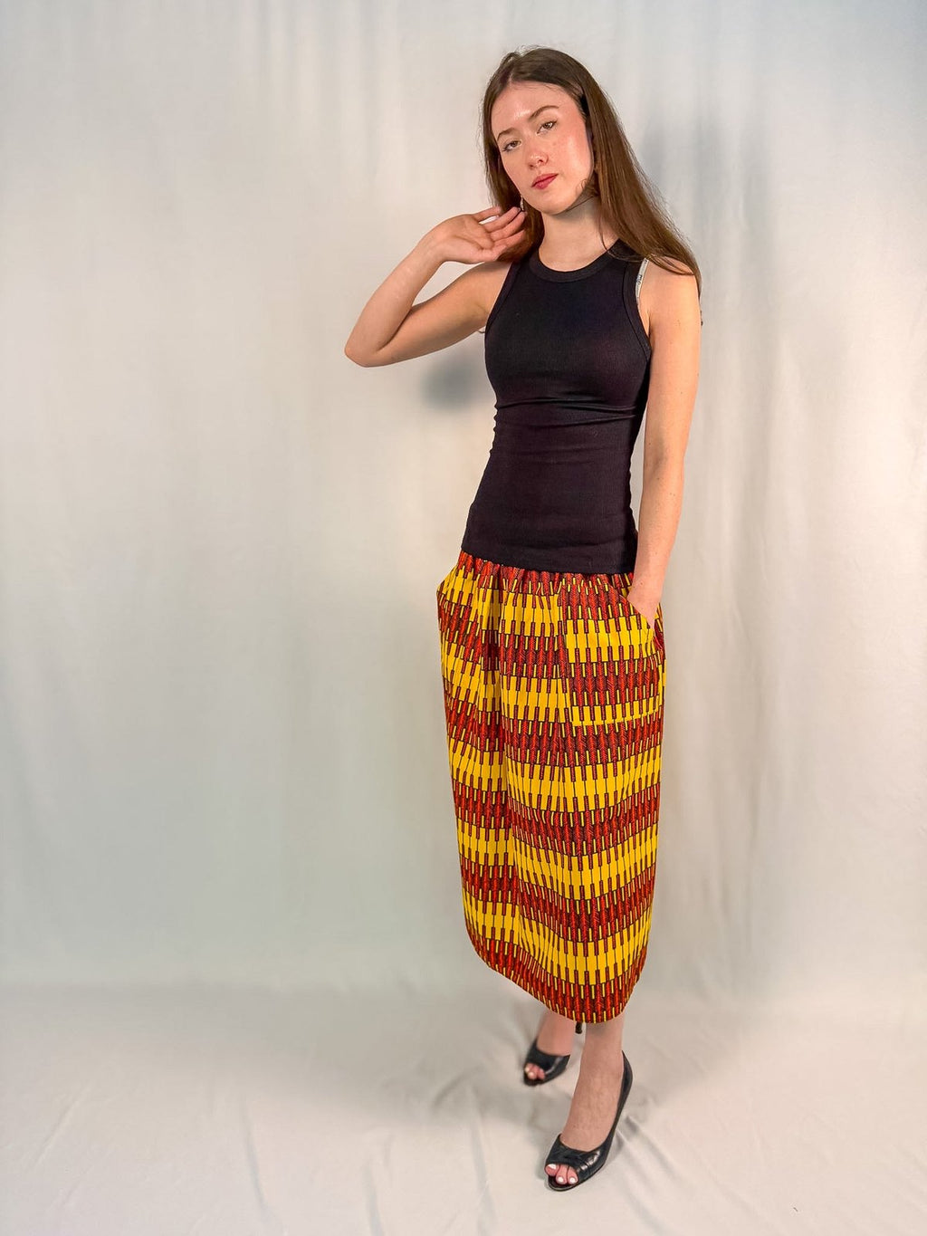 Woman wearing a black top and colorful skirt against a plain background onsem