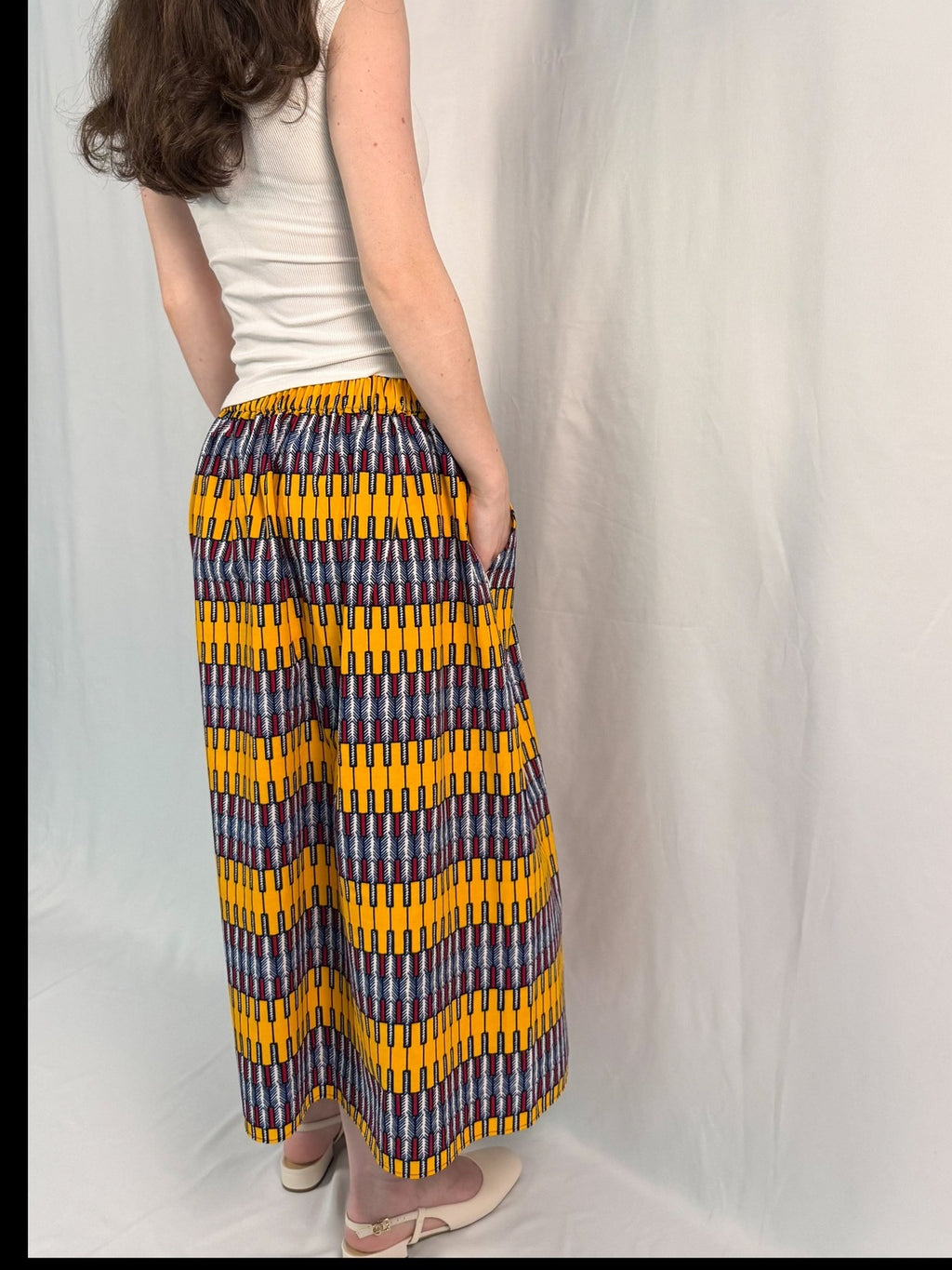 Person wearing a white sleeveless top and colorful patterned pants against a white background