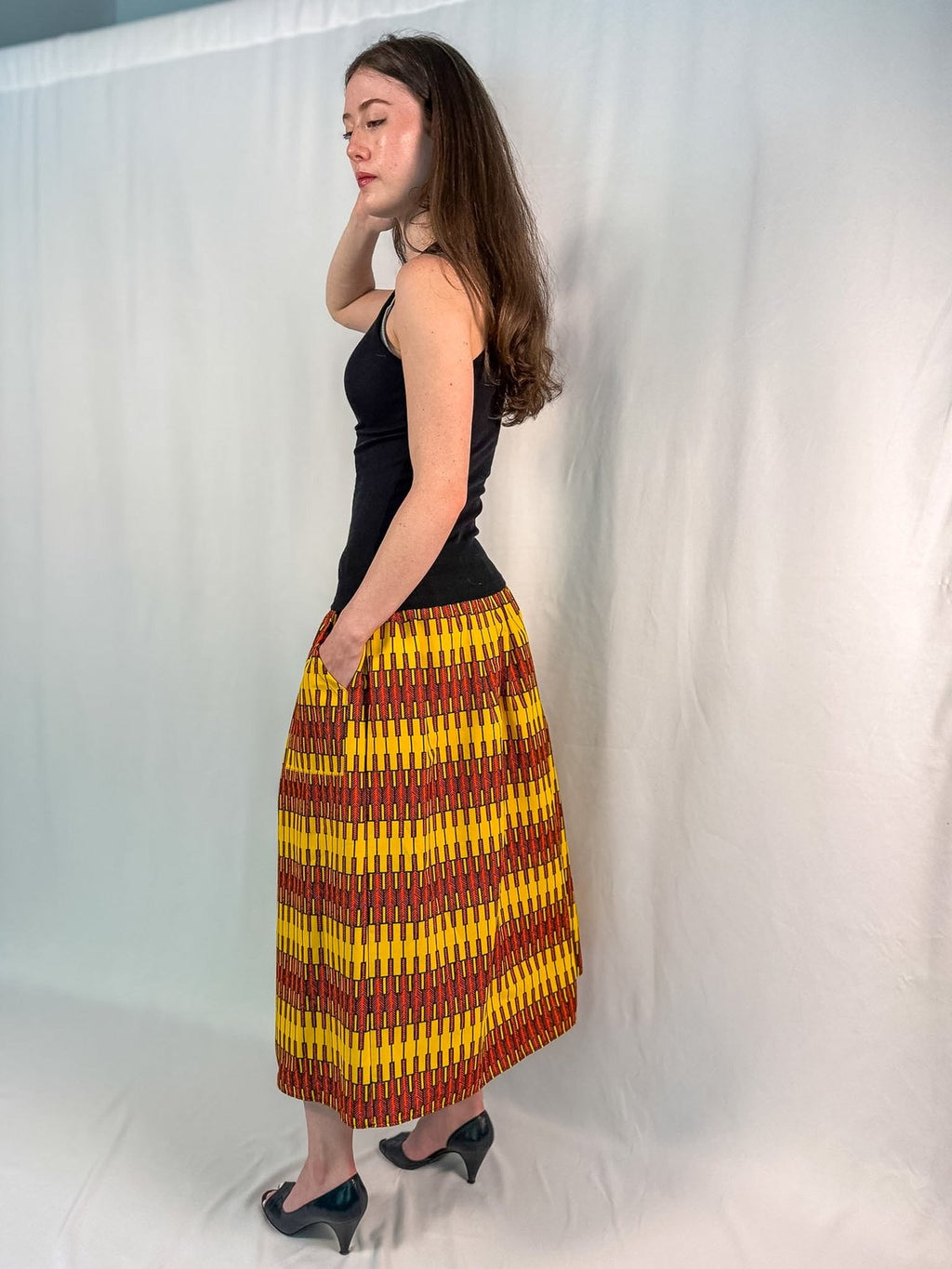 Woman wearing a black top and yellow patterned skirt against a white background - onsem