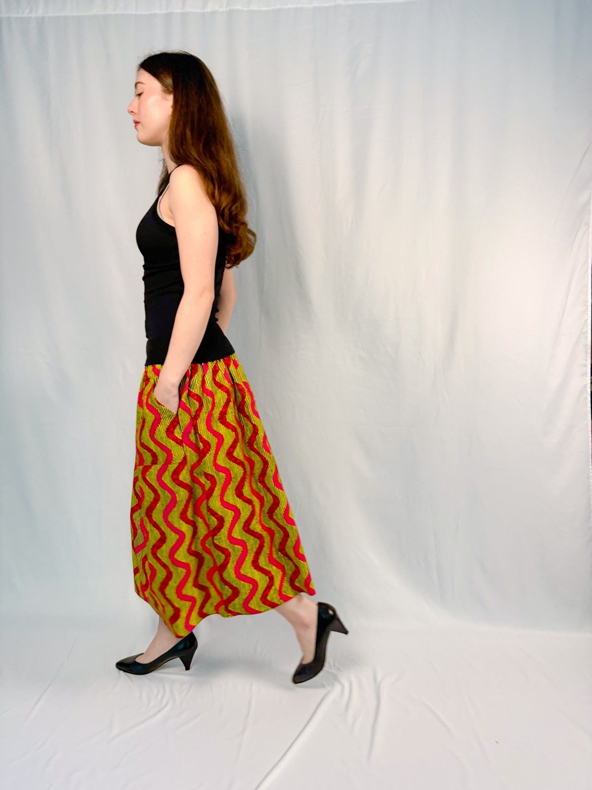 Woman wearing a black top and red and green patterned skirt on a white background onsem