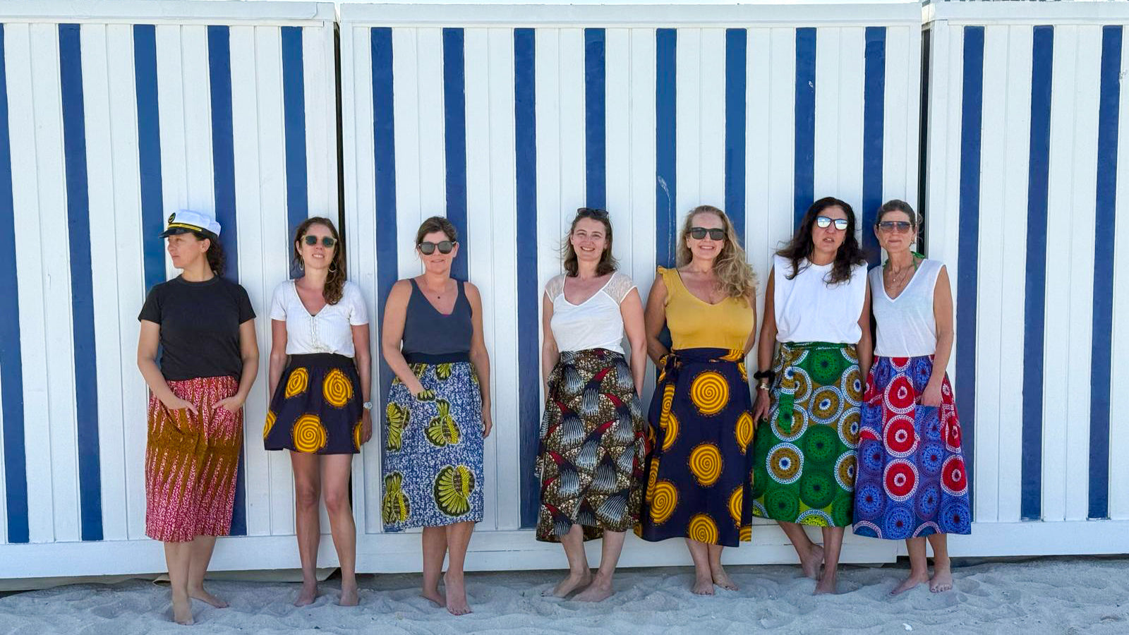 Group of women in colorful skirts standing in front of a blue and white striped wall.